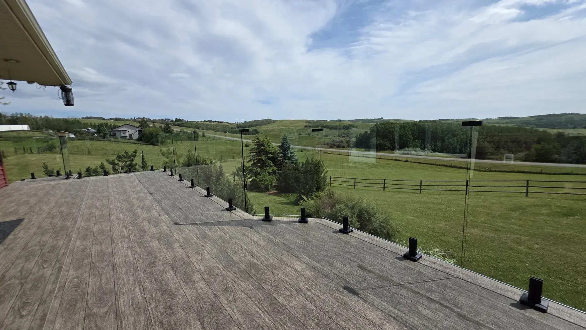 A wide woodgrain vinyl deck behind frameless glass, green foothills and open sky beyond