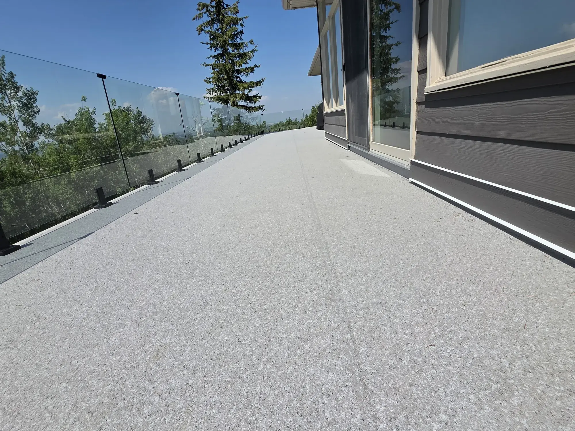 A granite vinyl deck running the length of the house behind glass railing, spruce and blue sky
