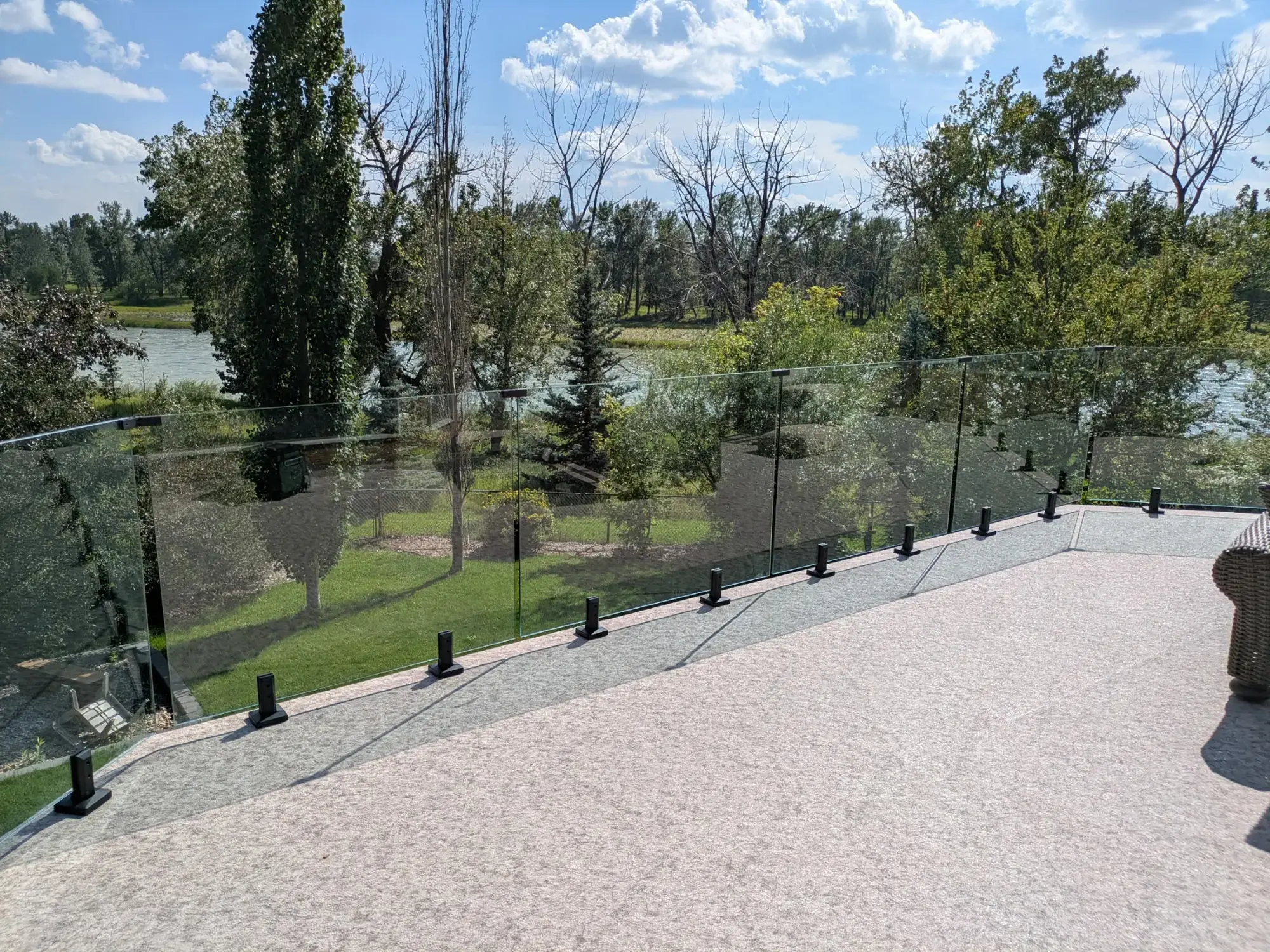 A pale granite vinyl deck with glass railing, looking across a pond and trees