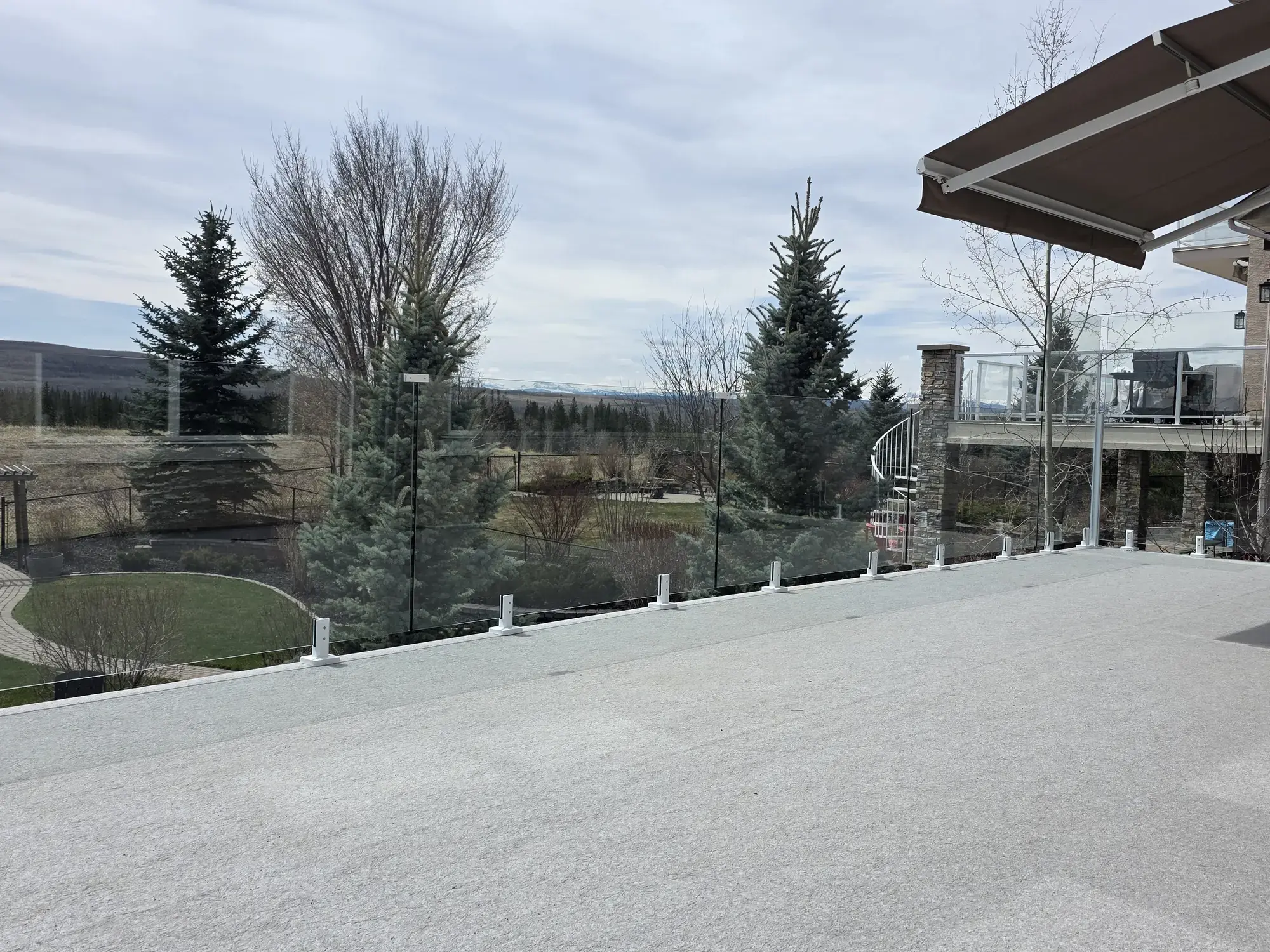 A vinyl deck with glass railing above a landscaped yard, spruce on both sides