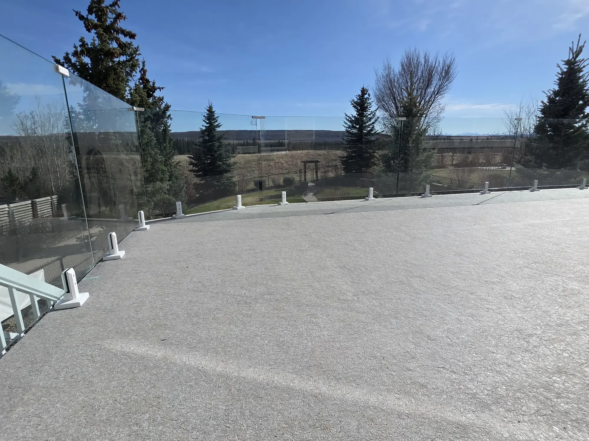 A pale granite vinyl deck behind glass railing with white posts, spruce and foothills beyond