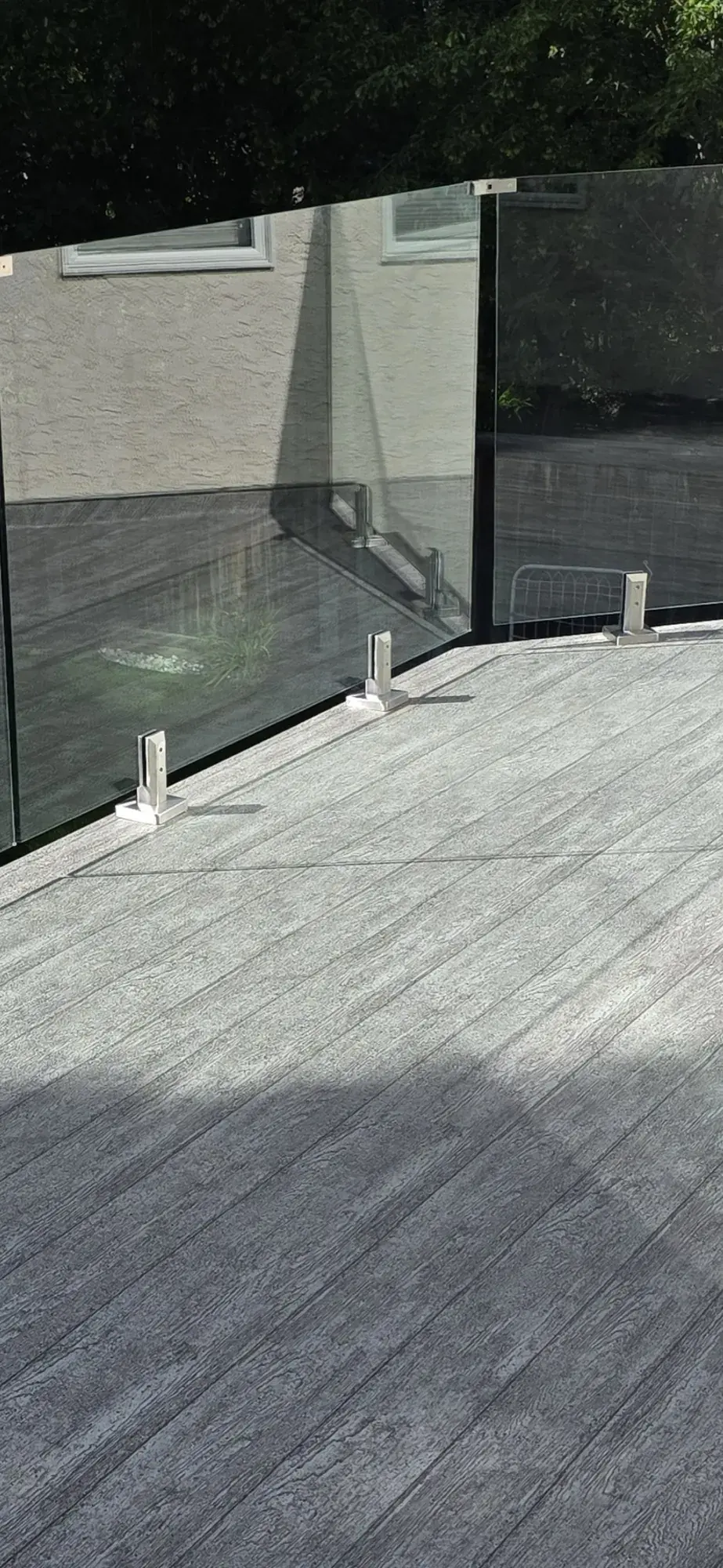 Grey woodgrain vinyl planking running under a frameless glass railing, stucco wall behind