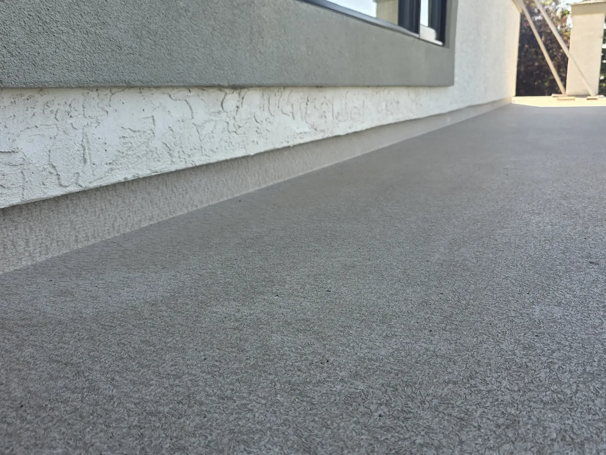 Close-up of a granite vinyl deck surface where it meets the stucco wall of the house