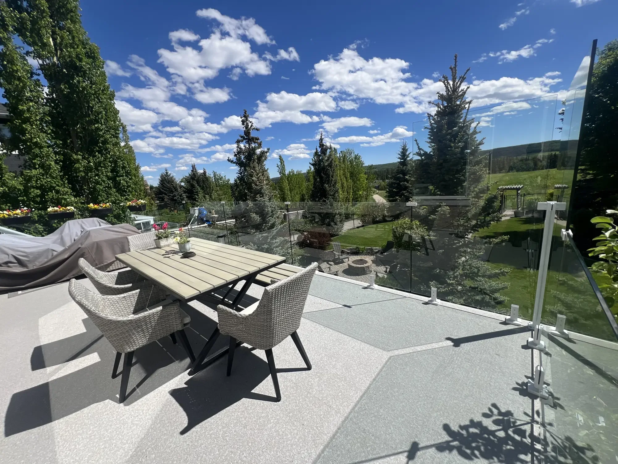 A furnished granite vinyl deck in full sun, table and chairs behind frameless glass, valley beyond